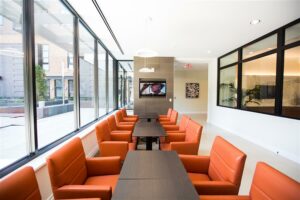 bright community room with tables, orange cushioned chairs and tv