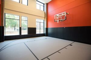 indoor basketball court with floor to ceiling windows, high ceilings, orange wall