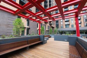 center courtyard with benches, wood paneled flooring, with bright red geometric pergola above