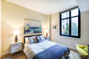 large bright bedroom facing wide window, carpeted flooring