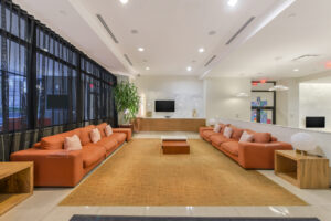 Interior Community Room, orange couches, contemporary area rug, tile floor, tv on wall, mid century modern furniture.