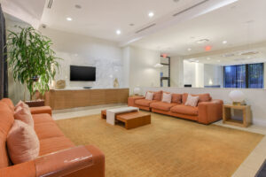 Interior Community Room, orange couches, contemporary area rug, tile floor, tv on wall, mid century modern furniture.