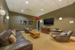 Interior theatre room, reclining seats, wood coffee table, olive colored walls, city photographs on the wall, tv on wall, city photographs on wall.