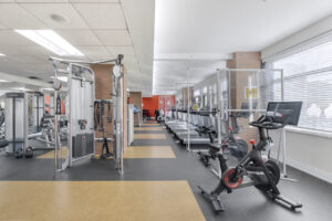 Interior Fitness Center, 2 peloton bikes, various weight lifting machines, multiple treadmills, windows with view of outside.