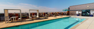 Exterior Rooftop Pool area, covered dining tables, lawn chairs, skyline in the background at sunset