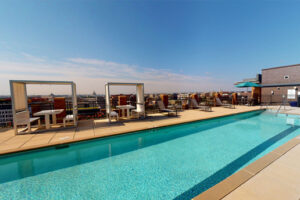 Exterior Rooftop Pool area, covered dining tables, lawn chairs, skyline in the background at sunset